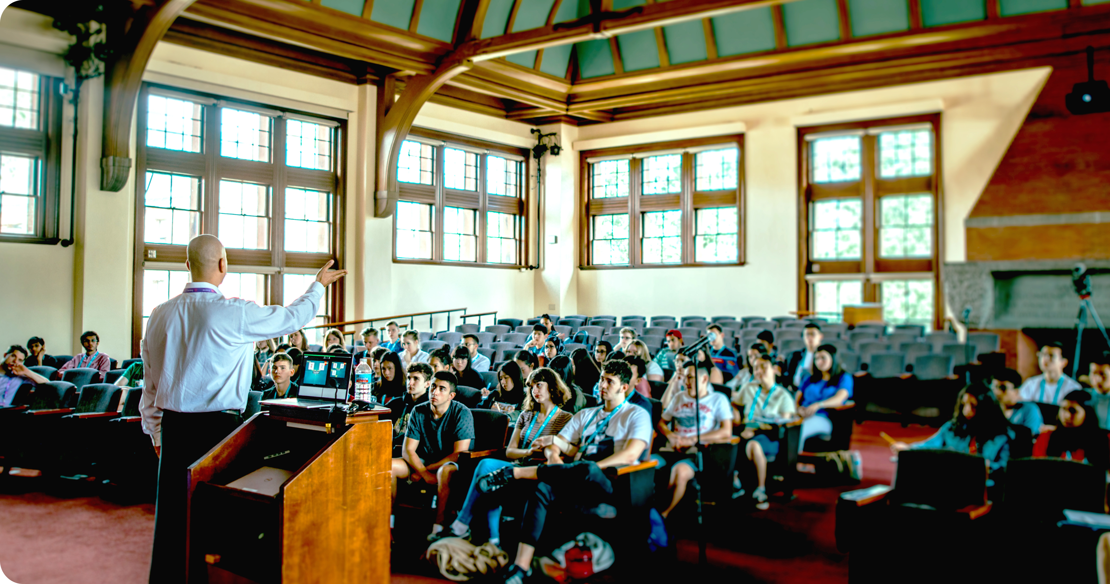 An engaging speaker leads a diverse group of attentive students in a historic lecture hall. Setting the tone for thoughtful conversations featured in our education podcast.